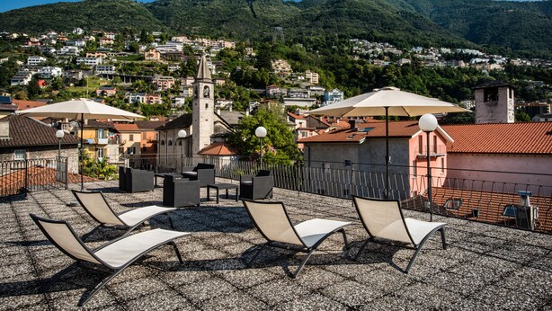 Terraza en la azotea con sillones de descanso, sombrillas y vistas a un pueblo en la ladera.