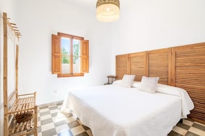 A bedroom with a large bed, wooden headboard, a window with wooden shutters, and a checkered floor.