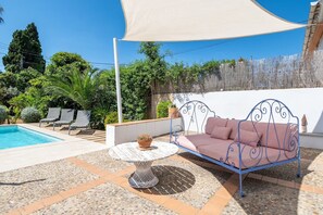 Une terrasse avec une piscine, un banc en métal, une table avec une plante et un espace ombragé.