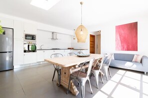 Une cuisine moderne avec des meubles blancs, des appareils en acier inoxydable, une table à manger en bois et un canapé bleu.