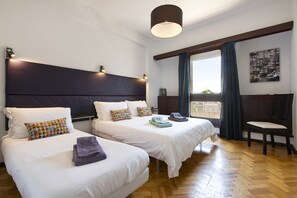 A hotel room with two beds, a large window with curtains, a chair, and a ceiling light.