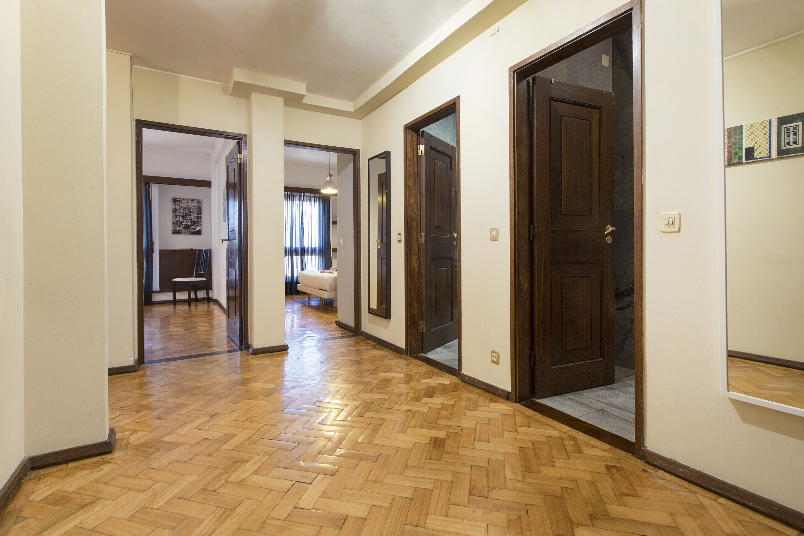 A hallway with wooden flooring, multiple doors, and a light fixture.