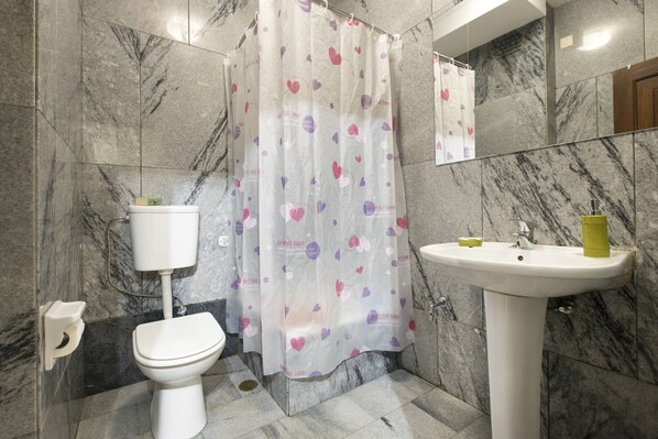 A bathroom with a toilet, a shower curtain with heart patterns, a sink, and marble walls.