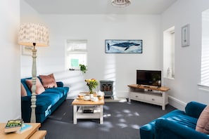 Een moderne woonkamer met een blauwe bank, een salontafel, een televisie en een open haard.