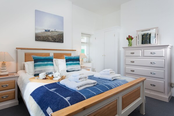 A hotel room with a bed, a bedside table with a lamp, a dresser with drawers, a mirror, and a painting on the wall.