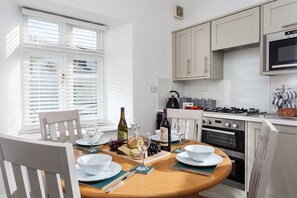A modern kitchen with white cabinetry, a dining table set for two, and a window with blinds.