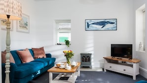 A modern living room with a blue sofa, a coffee table with a vase of flowers, a television, and a fireplace.