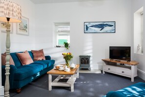 Een moderne woonkamer met een blauwe bank, een bijzettafeltje met een bloevas, een televisie en een open haard.