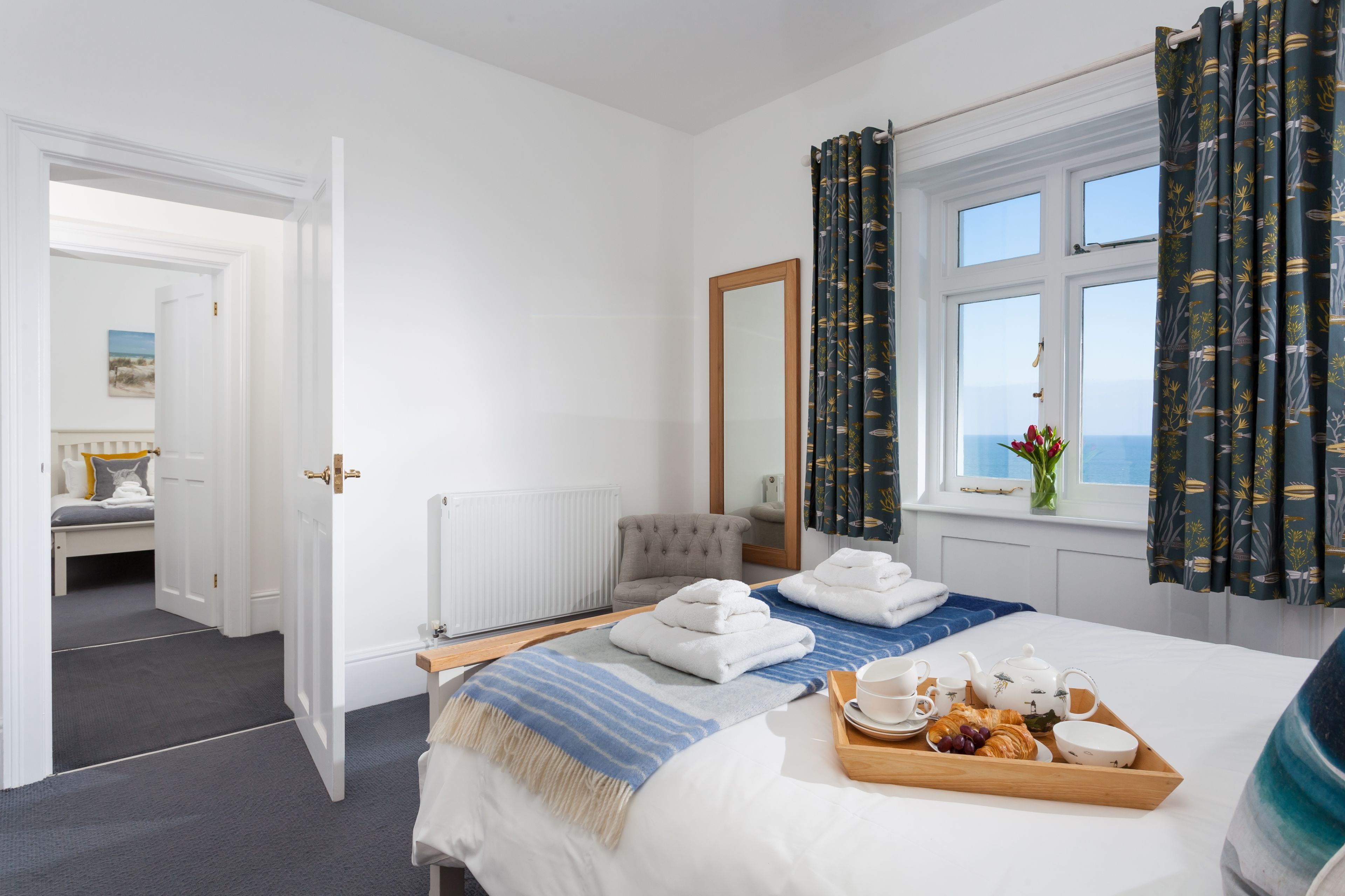 Ein Hotelzimmer mit Bett, Nachttisch, Spiegel, Fenster mit Vorhängen und Meerblick.