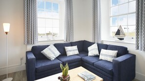 A modern living room with a blue sectional sofa, patterned curtains, a floor lamp, and a small plant on a wooden coffee table. - Ariel, Marcross, Llantwit Major , Vale of Glamorgan, Wales (Marcross)