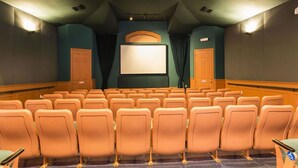 Cinema com fileiras de assentos laranja, uma tela grande e um projetor.