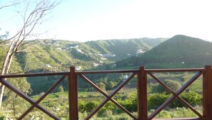 A scenic view from a wooden deck overlooking a valley with scattered houses and lush greenery. - Casa Rural Las Caldereras (Teror)