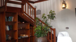 A wooden staircase with a bookshelf on the left, a potted plant in the center, and a white chair on the right. - Casa Rural Las Caldereras (Teror)