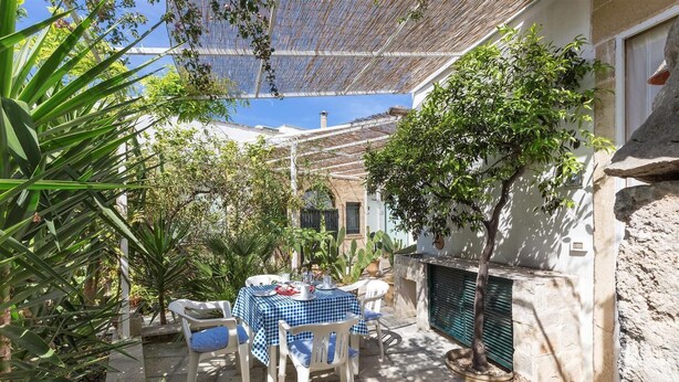 Un patio exterior con una mesa y sillas a cuadros, rodeado de plantas y una pérgola.