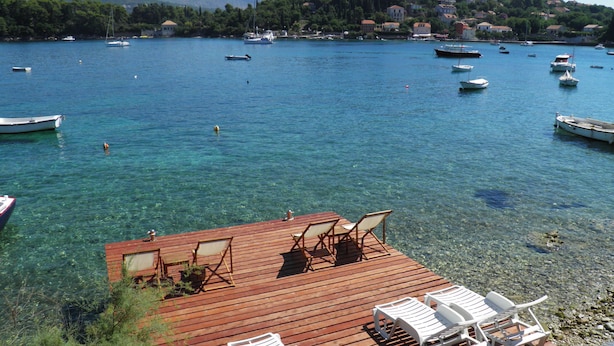 Une terrasse en bois donnant sur une eau d’un bleu limpide, avec des bateaux et une ville qui se dessine à l’horizon.