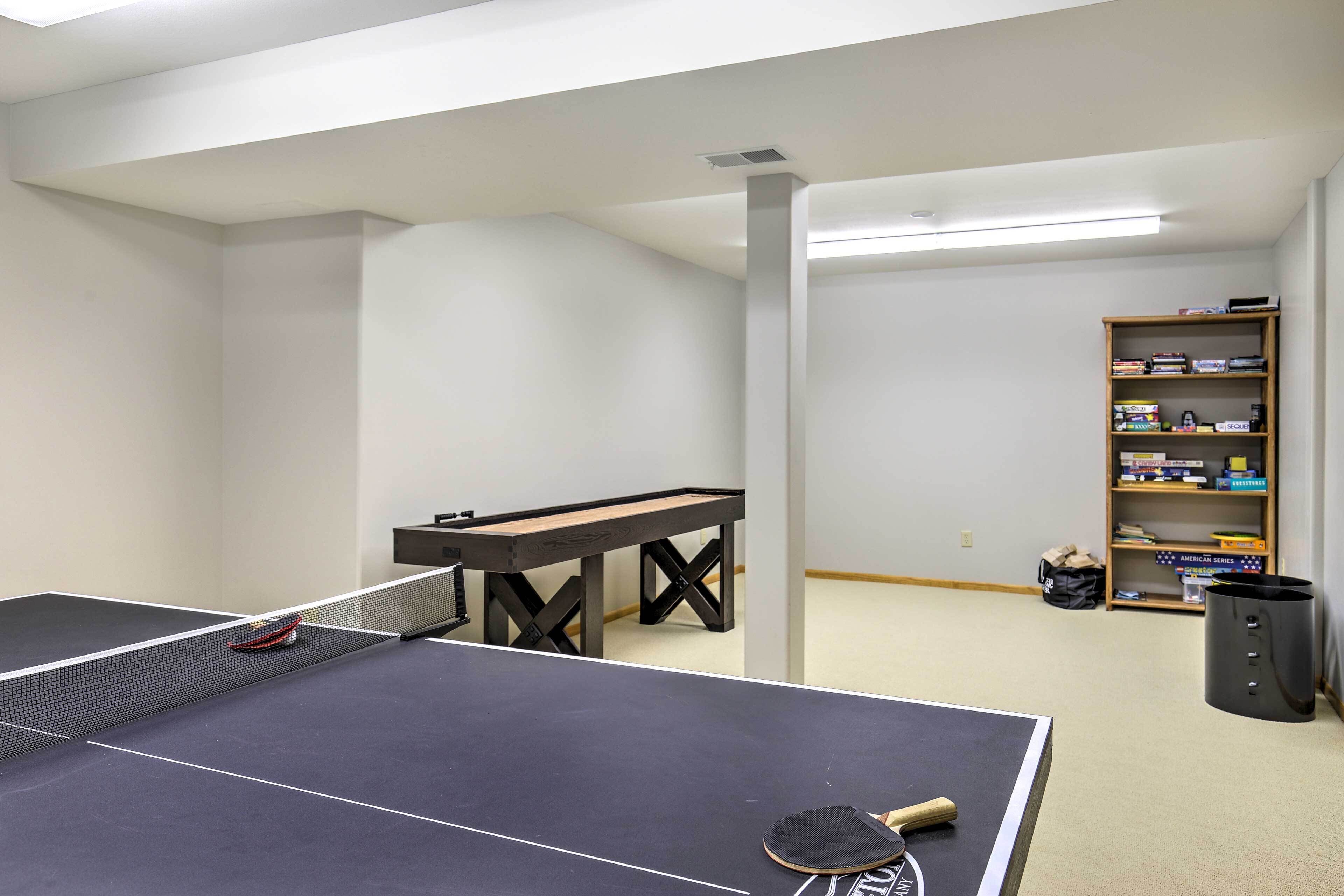Ein Tischtennistisch mit Schläger, ein kleiner Tisch und ein Bücherregal in einem Raum mit weißen Wänden und Teppichboden.