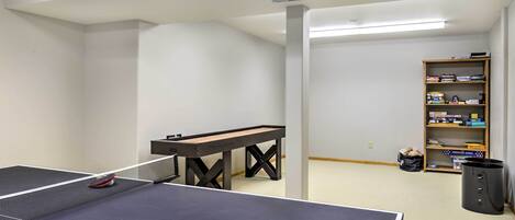 Ein Tischtennistisch mit Schläger, ein kleiner Tisch und ein Bücherregal in einem Raum mit weißen Wänden und Teppichboden.