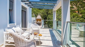 Ein Balkon mit Korbmöbeln, einem Tisch mit Getränken und Früchten sowie Blick auf eine gebirgige Landschaft.