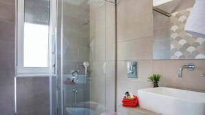 Ein modernes Badezimmer mit einer begehbaren Glasdusche, einer weißen Toilette und einem großen, weißen Waschbecken.