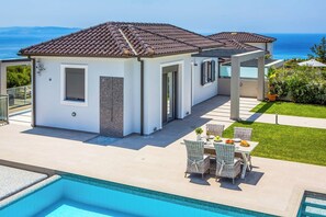 En modern villa med pool, utomhusmöbler och utsikt över havet.