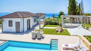Eine moderne Villa mit Pool, Sitzgelegenheit im Freien und Meerblick.