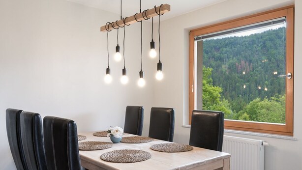 A dining area with a wooden table, black chairs, and a view of a forest through a large window.