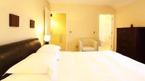 Een slaapkamer met een bed, een stoel, een dressoir en een deur naar een badkamer.