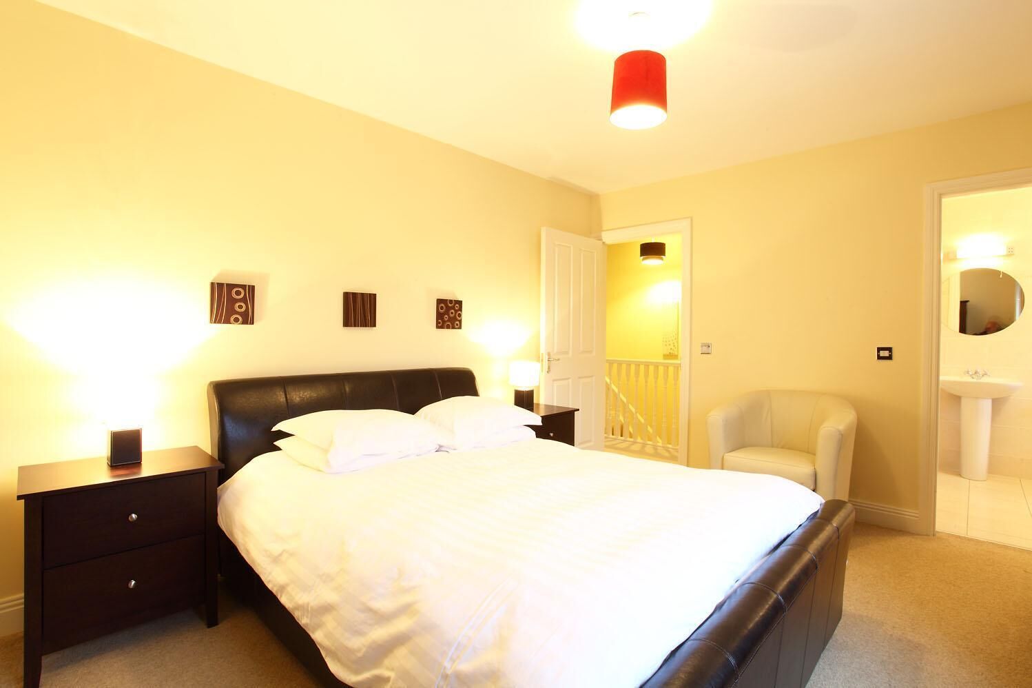 Ein Hotelzimmer mit einem großen Bett, einem Nachttisch, einem Sessel und einem Badezimmer mit Waschbecken und Spiegel.