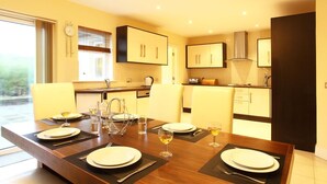 Een moderne keuken met een eethoek, met een grote tafel gedekt voor vier personen, een raam met zonwering en inbouwkeukenmeubels.
