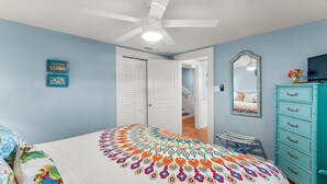 A bedroom with a ceiling fan, a bed with a colorful bedspread, a dresser, and a mirror on the wall. - Unit 71, Catch of The Day, 3 Bedroom Beach Condo (Panama City Beach)
