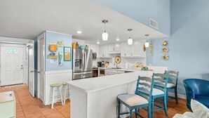 A modern kitchen with white cabinets, a stainless steel refrigerator, and a central island with bar stools. - Unit 71, Catch of The Day, 3 Bedroom Beach Condo (Panama City Beach)