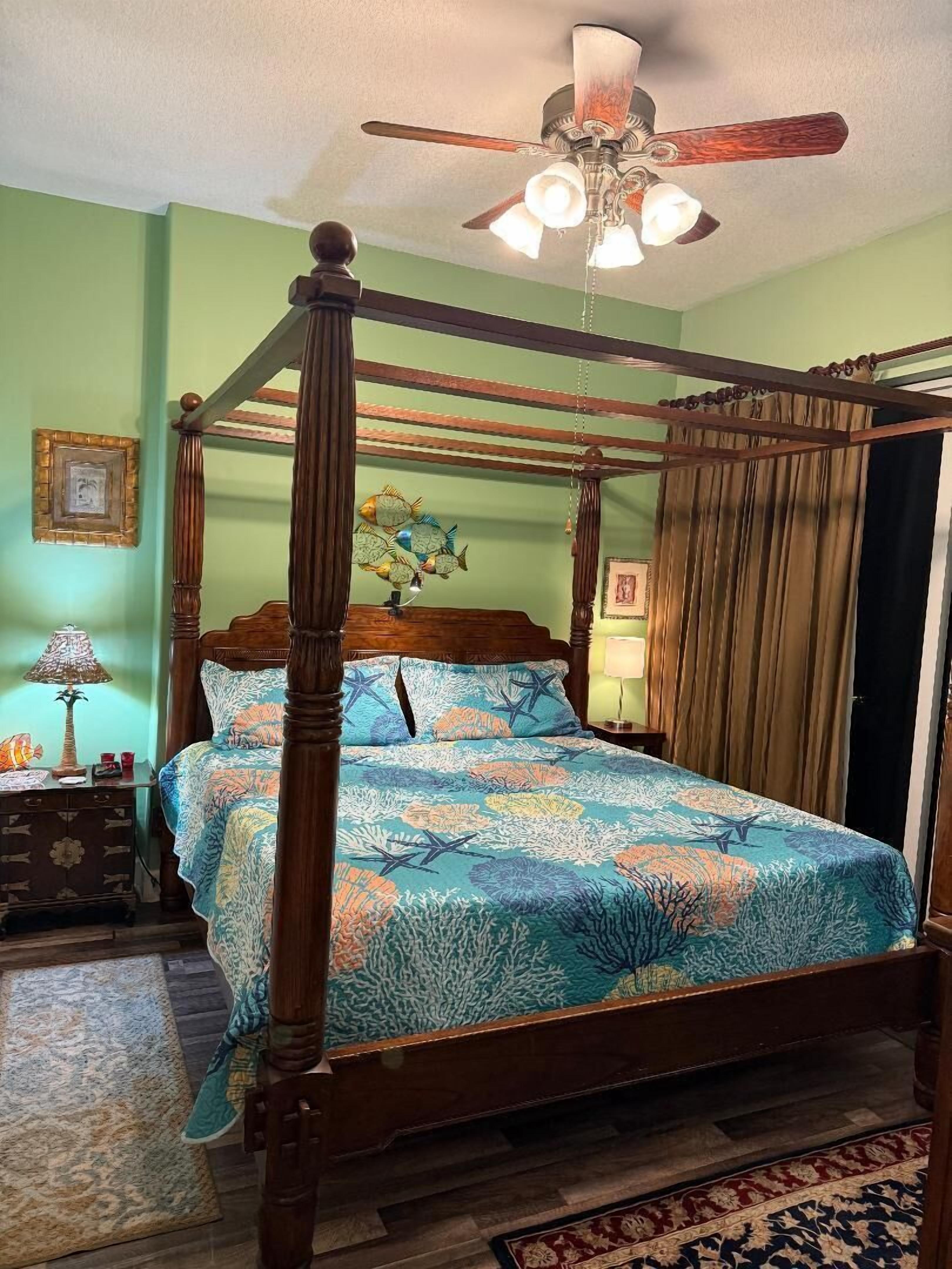 A four-poster bed with a canopy, a ceiling fan, and a nightstand with a lamp.