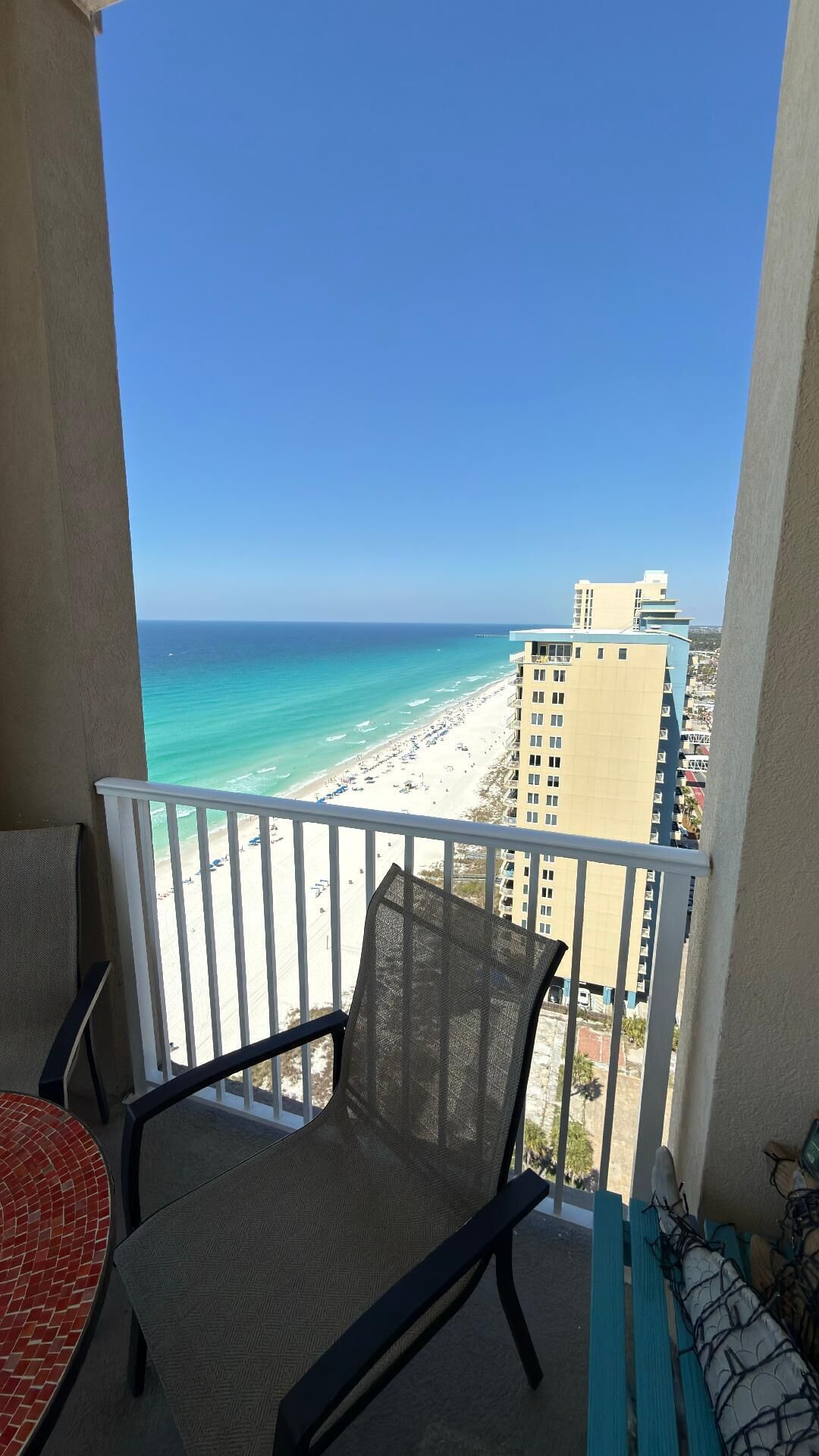 A balcony with a view of a beach and ocean, a chair, and a table.