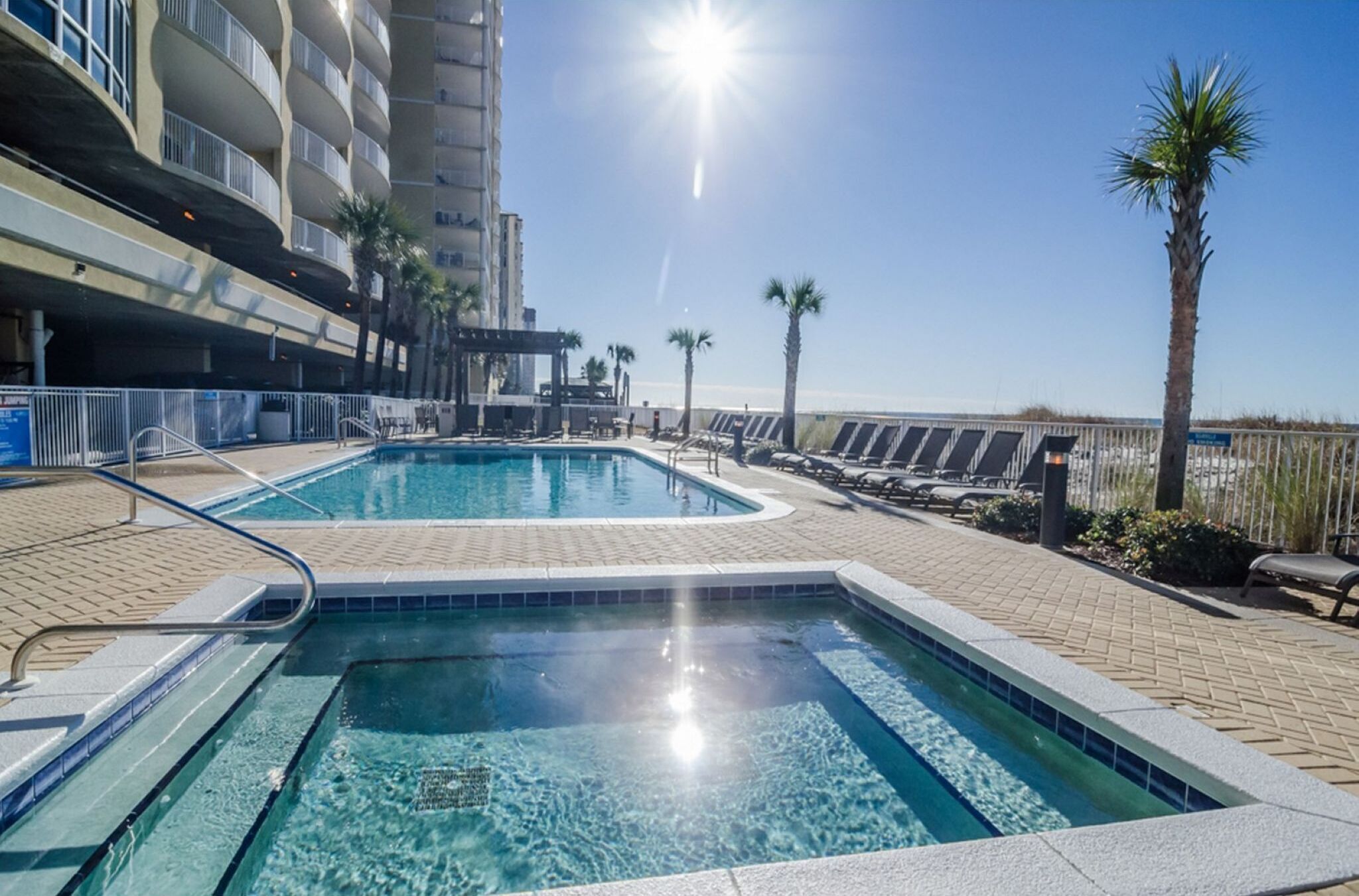 A swimming pool with a sunlit view of a beach and palm trees.
