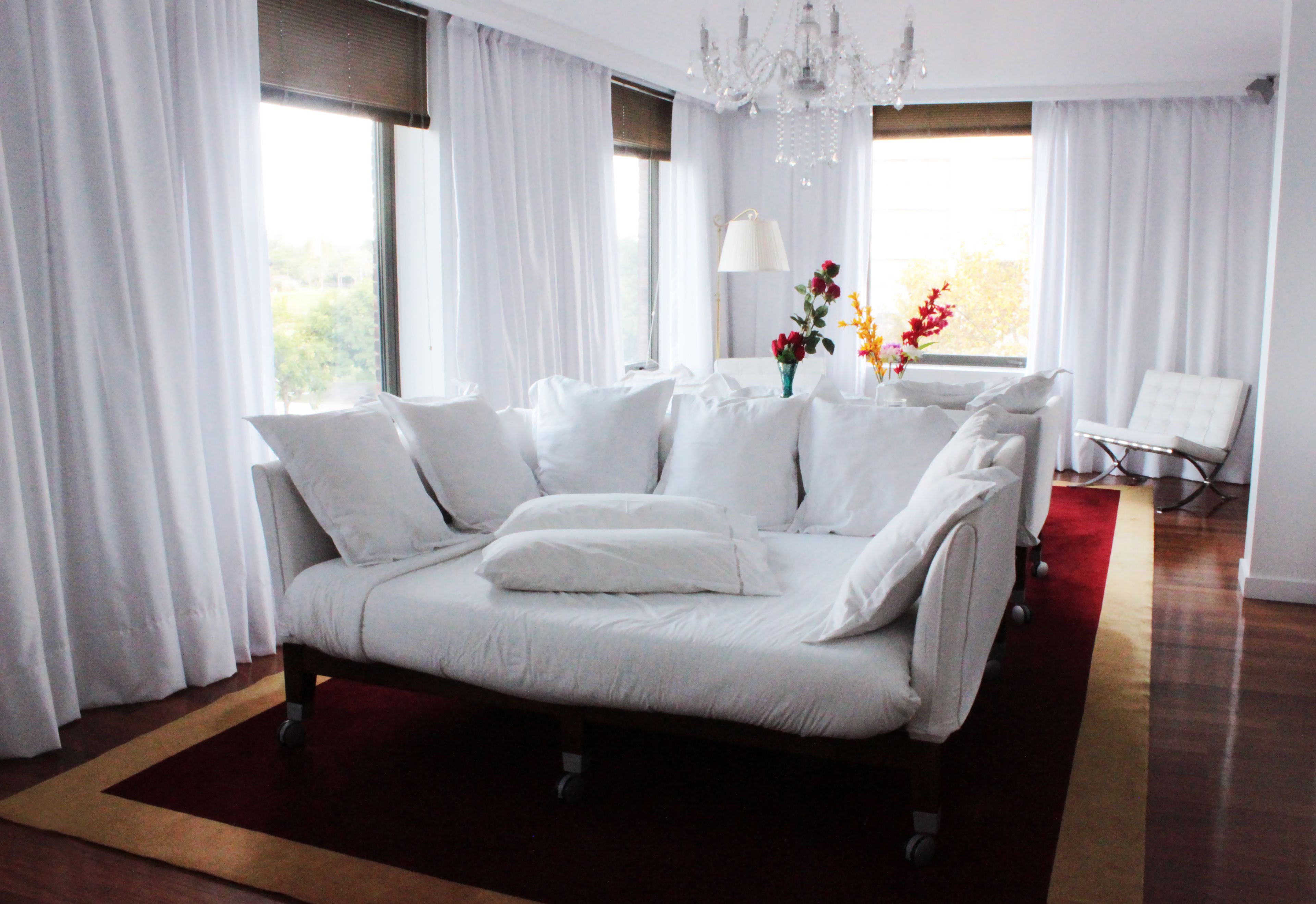 A modern living room with a white sofa, a chandelier, and a view of the outdoors through large windows.