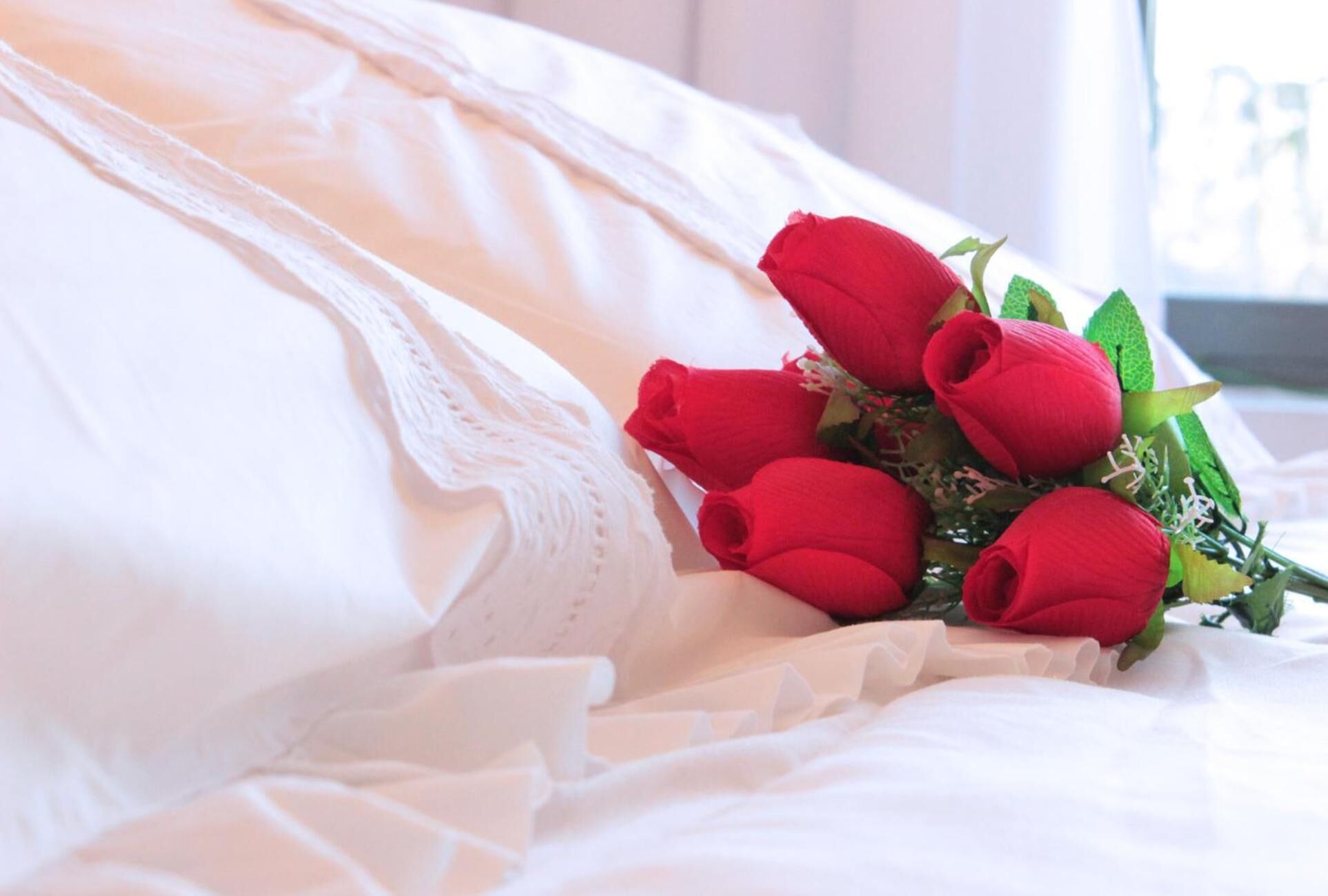 A bed with white linens and a bouquet of red roses.
