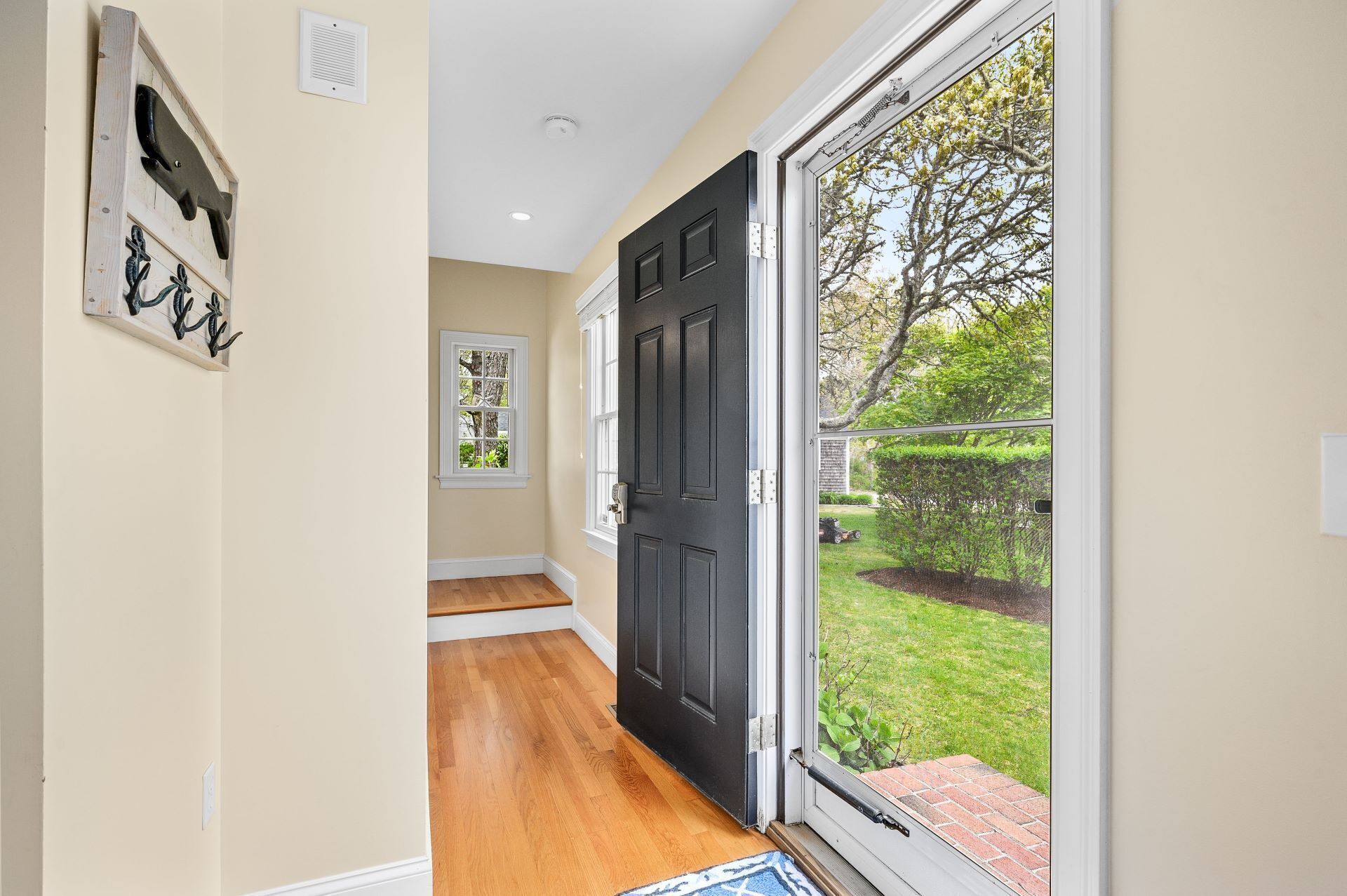 A hallway with a black door, a window, and a doorbell.