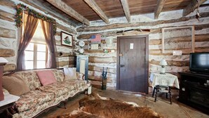 L’intérieur d’un chalet rustique en rondins de bois, avec un canapé, un téléviseur et un tapis en peau de vache.