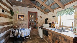 Une cuisine rustique avec des murs en pierre, des poutres en bois, une table à manger avec des chaises et un évier encastré.
