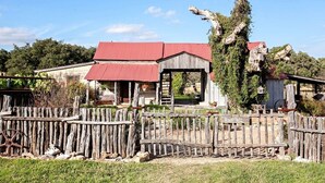 Une cabane en bois rustique, avec un toit rouge, entourée d’une clôture en bois et d’un grand arbre.