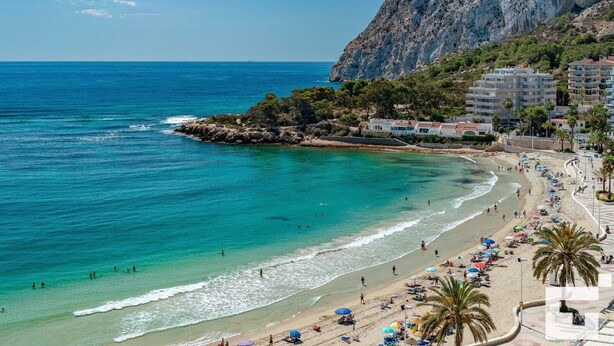 A coastal beach with clear turquoise waters, a rocky outcrop, and a row of buildings with balconies overlooking the sea. - Zafiro 35C - Grupo Turis - Calpe, Costa Blanca (Calpe)