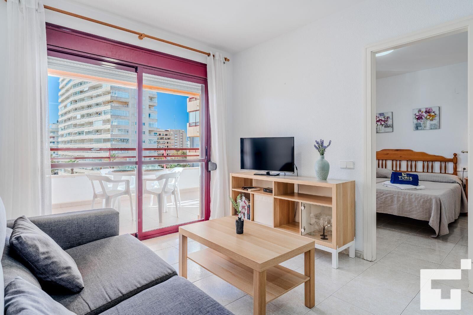 A modern living room with a sofa, a TV on a wooden stand, and a balcony with a city view.