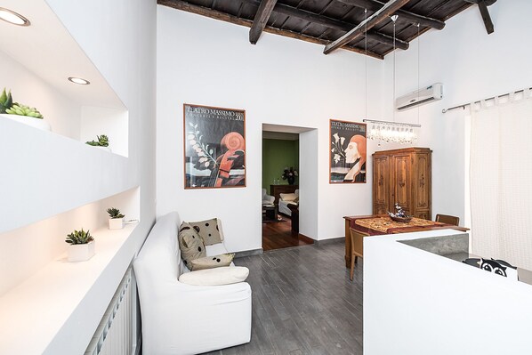 Un interior moderno con un sofá blanco, una mesa de madera con un cuenco decorativo y dos carteles en las paredes.