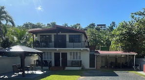 A two-story house with a balcony, a covered patio, and a fenced yard. - Kasa Maui - Ocean View Apartment - 1 Minute From Sandy Beach!! (Rincon)