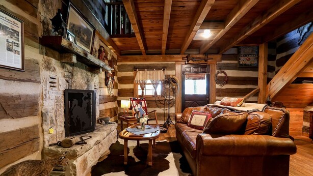 Interior rústico de cabaña con chimenea de piedra, sofá de cuero y vigas de madera.