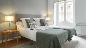 Moderni hotellihuone, jossa on suuri sänky, kaksi yöpöytää, kuvioitu seinä ja näkymä rakennuksiin ikkunasta.
