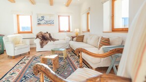 En rummelig stue med et stort vindue, træloft og et hyggeligt opholdsområde med et fletstæppe.