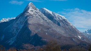 Una montaña con cima nevada, rodeada por un valle con vegetación escasa y algunos edificios.