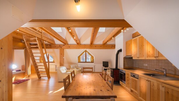 Un loft amplio con una mesa de comedor de madera, zona de cocina y un dormitorio en loft con tragaluz.