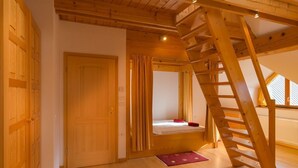 Una habitación con una escalera de madera, una puerta y una cama con un cojín rojo.